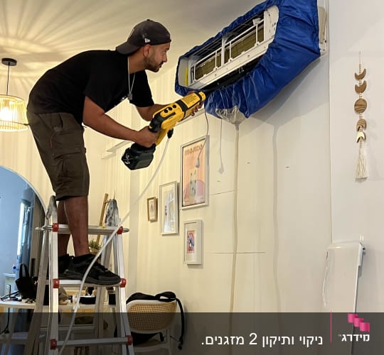 אדם מנקה מזגן עם מכשיר חשמלי על סולם